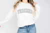 a woman wearing a white sweatshirt with the word teacher printed on it