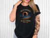a woman wearing a black t - shirt with the eclipse in the background
